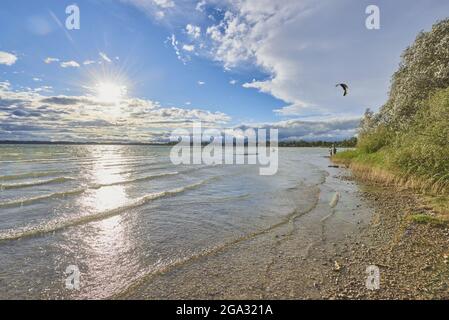 Chiemsee, mit hellem Sonnenlicht auf der Wasseroberfläche reflektiert und ein Kitesurfer in der Nähe des Ufers; Bayern, Deutschland Stockfoto