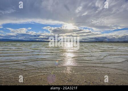 Chiemsee, mit hellem Sonnenlicht, das auf der Wasseroberfläche bis zum Ufer reflektiert wird; Bayern, Deutschland Stockfoto