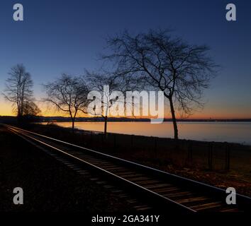 Das Licht am frühen Morgen beleuchtet die Küste und die Bahngleise, die entlang des Wasserrands in White Rock, BC, und White Rock, British Columbia, Kanada, führen Stockfoto