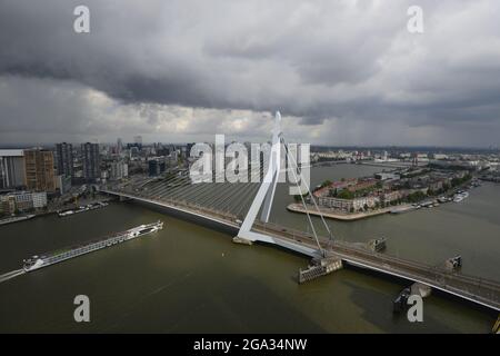 Vogelperspektive auf die Erasmus-Brücke und die Skyline von Rotterdam in den Niederlanden. Ein Kreuzschiff fährt unter der Brücke vorbei und Gewitterwolken sind über der Brücke Stockfoto