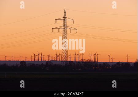 Strommasten und Windturbinen auf dem Land bei Sonnenuntergang; Biebesheim am Rhein, Hessen, Deutschland Stockfoto