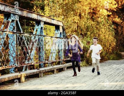 Ein Bruder und eine Schwester, die über eine Brücke laufen und während der Herbstsaison in einem Stadtpark Zeit miteinander verbringen Stockfoto