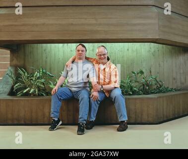 Zwei Männer mit Down-Syndrom sitzen zusammen und zeigen Zuneigung; Deutschland Stockfoto