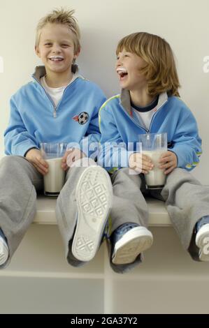 Zwei Jungen sitzen in passenden Outfits mit vollen Gläsern Milch und Milchburen; Deutschland Stockfoto