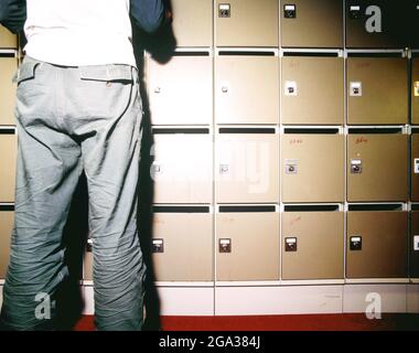 Mann, der an einer Wand mit Safe-Einlagen mit einem Schlüssel zum Öffnen eines Schließfachs steht; Deutschland Stockfoto