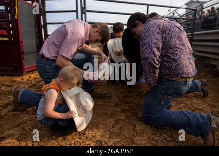 3. Juli 2021; Bloomington, Indiana: Ein Junge betet mit einer Gruppe von Rodeo-Teilnehmern vor dem 3 Bar J Rodeo, 2. Juli auf der Monroe County Fair. Der Vater des Jungen ritt im Rodeo. Stockfoto