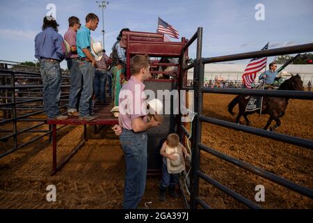 3. Juli 2021; Bloomington, Indiana: Ein Junge hört mit einer Gruppe von Rodeo-Teilnehmern vor dem 3 Bar J Rodeo am 2. Juli auf der Monroe County Fair das Spielen der Nationalhymne. Der Vater des Jungen ritt im Rodeo. Stockfoto