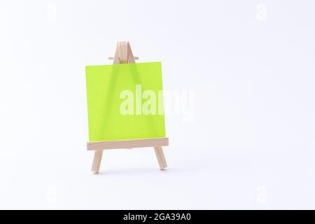 Miniatur aus Holz mit quadratischer Leinwand oder Notizpapier - Mockup. Mini-Holzständer mit sauberer Zeichenfläche auf weißem Hintergrund, Copy Space Stockfoto