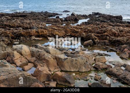 Blauer Himmel und Meer über den Felsen und Sand am Strand. Wellen krachen auf die Felsen und Sand am Strand. Stockfoto