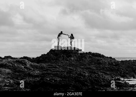 Silhouette von zwei Personen auf einem sehr großen Felsen. Ondina Beach in Salvador, Bahia, Brasilien. Stockfoto