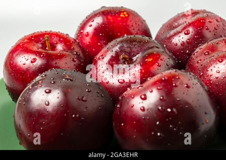 Blick von der Seite der großen roten Pflaumen auf dem grünen Teller. Stockfoto