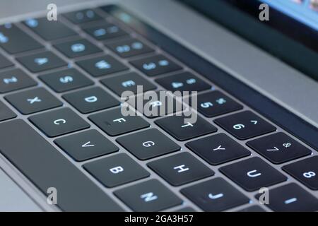 Nahaufnahme von Makroaufnahmen mit einer geringen Schärfentiefe einer Computertastatur mit schwarzen Tasten, weißen Buchstaben und grauem Gehäuse, mit Tasten, die mit blauem Licht hinterleuchtet sind Stockfoto