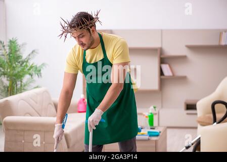 Junger männlicher Auftragnehmer, der auf dem Kopf einen stacheligen Kranz trägt und Hausarbeit leistet Stockfoto