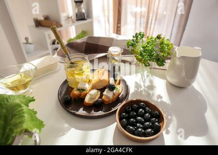 Teller mit leckeren Bruschettas mit Feta-Käse und Zutaten auf dem Tisch in der Küche Stockfoto