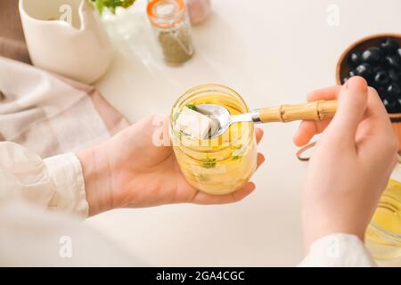 Frau nimmt ein Stück leckeren Feta-Käse aus dem Glas auf dem Tisch in der Küche, Nahaufnahme Stockfoto
