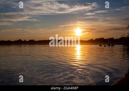 Ein farbenfroher, sonniger Sonnenuntergang spiegelt sich auf der Oberfläche des ruhigen Sees wider. Stockfoto