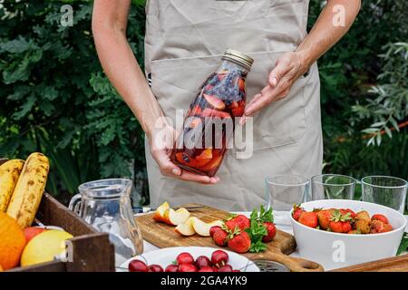 Frauenhand hält eine erfrischende hausgemachte Limonade oder Sangria Punsch mit Zitrusfrüchten und Bio-Beeren. Sommercocktail mit Eis und Fruchtsaft in einem Stockfoto