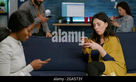 Multirassische Freunde, die getrennt auf der Couch sitzen, surfen im Internet und sehen sich Online-Serien an. Gruppe von Menschen mit gemischter Rasse, die spät in der Nacht im Wohnzimmer Zeit miteinander verbringen Stockfoto