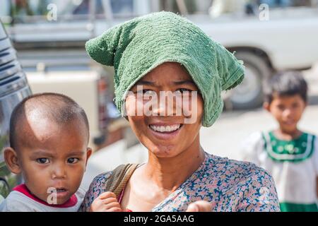 Hübsche junge burmesische Mutter mit Handtuch auf dem Kopf hält Kind in den Armen, Mandalay, Myanmar Stockfoto