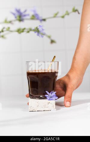 Chicorée Drink in einem transparenten Becher mit Chicorée Blumen im Vordergrund. Stockfoto