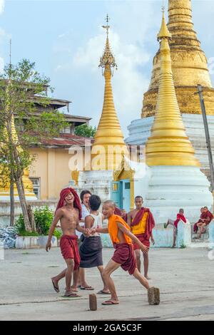 Eine Gruppe junger burmesischer Mönche in kastanienbraunen Roben, die neben goldenen Stupas in der Pagode/Tempel, Kalaw, Myanmar, Fußball spielen Stockfoto