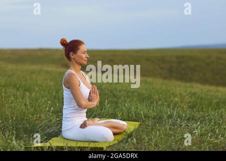 Die junge Frau praktiziert Yoga und Meditation und sitzt in Lotusposition draußen vor der Stadt. Stockfoto