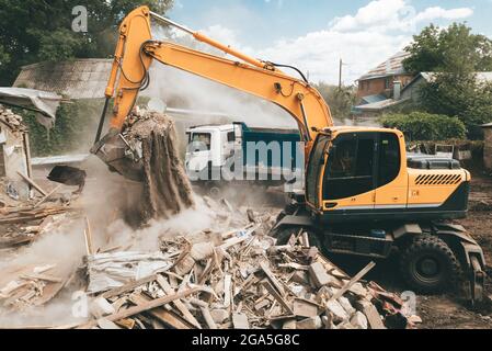 Bagger belädt Bauabfälle zur Entfernung in den LKW. Abriss des Hauses. Zerstörung von Gebäuden. Aufräumarbeiten von Flächen für die Entwicklung und Neubauten. Stockfoto