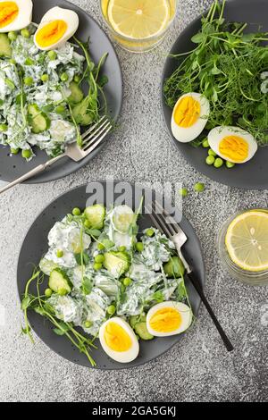 Salat mit Rucola, Gurken und jungen Erbsen mit Joghurt und gekochten Eiern mit Microgreens, Zitronenwasser im Glas, Draufsicht Stockfoto