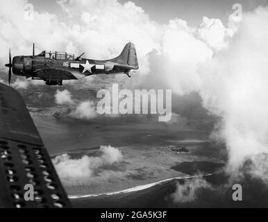 Pazifikkrieg: Ein US-amerikanischer Sturzbomber Douglas SBD Dauntless fliegt am 15. Juni 1944 über die Insel Saipan. Die Schlacht von Saipan (15. Juni bis 9. Juli 1944) war eine Schlüsselschlacht im Pazifik während des Zweiten Weltkriegs, die zwischen den Streitkräften der Vereinigten Staaten und Japan ausgetragen wurde. Stockfoto