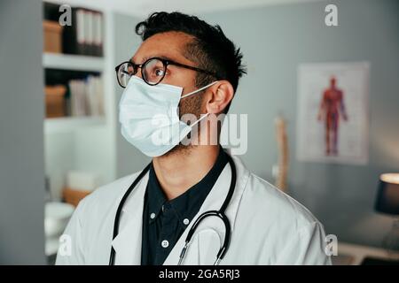 Gemischter männlicher Arzt, der in der Klinik mit einer chirurgischen Maske arbeitet Stockfoto