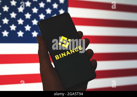 Binance-App-Logo auf dem Smartphone in der Hand mit verschwommenem Hintergrund amerikanischer Flagge. Binance in den USA Nachrichten. Krypto-Börse, Handelsplattform. Swansea, Großbritannien - 27. Juli 2021. Stockfoto