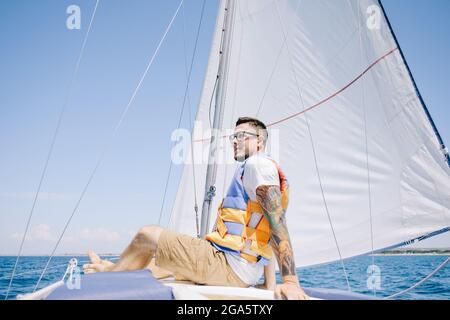 Glücklicher männlicher Reisender sitzt auf dem Bug der Yacht. Stockfoto