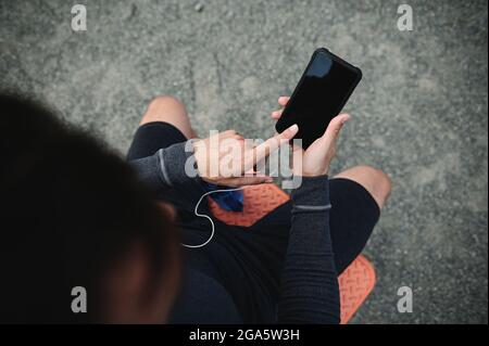 Aus dem hohen Winkel betrachtet zeigt ein Sportler, der mit dem Zeigefinger auf einen leeren Bildschirm eines Smartphones in der Hand zeigt. Speicherplatz für mobile Anwendung kopieren Stockfoto