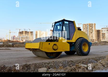 Vibration Einzylinder-Straßenwalze Nivellierboden für den Bau der neuen Asphaltstraße. Straßenarbeiten und Straßen reparieren.Turmkrane in Aktion bei c Stockfoto