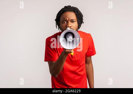 Mann mit Dreadlocks trägt ein rotes T-Shirt im lässigen Stil, hält das Megaphon in der Nähe des Mundes und spricht laut, schreit, kündigt an, achtet darauf. Stockfoto