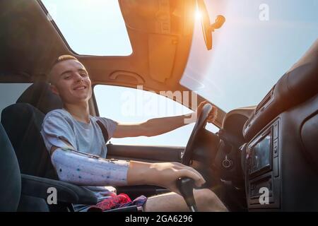 Der junge Kaukasusmann mit einem amputierten Arm und Prothese fährt ein Auto Stockfoto