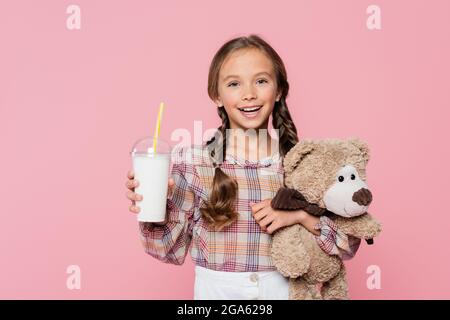 Glücklich präteen Kind hält weiches Spielzeug und Milchshake isoliert auf rosa Stockfoto