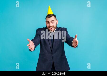 Komm in meine Arme! Freundlicher Mann im offiziellen Stil Anzug und Party-Kegel geben freie Umarmungen mit ausgestreckten Händen, einladend einladend zu umarmen. Innen Stockfoto