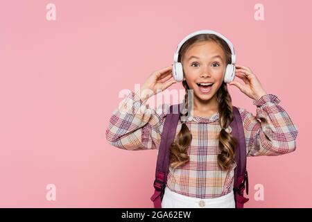 Aufgeregt Mädchen mit Rucksack hält Kopfhörer isoliert auf rosa Stockfoto