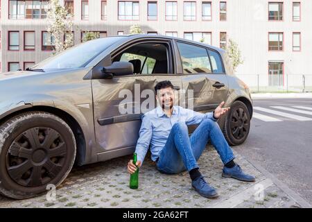 Junger Erwachsener verärgert Fahrer Mann mit Jeans und blauem Hemd sitzt in der Nähe von Crash-Auto, Kollisionsunfall in der Stadt Straße, nicht betrunken fahren, beschädigte Autotür Stockfoto