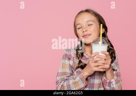 Zufrieden präteen Mädchen mit geschlossenen Augen halten Milchshake isoliert auf rosa Stockfoto