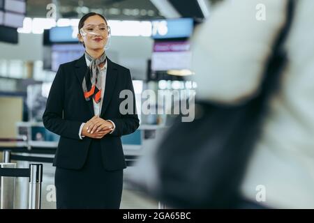 Flugbegleiter mit Gesichtsschutz, der am Flughafen steht. Flughafenmitarbeiter während einer Pandemie begrüßen Reisende. Stockfoto