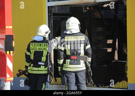 Quedlinburg, Deutschland. Juli 2021. Feuerwehrleute stehen vor dem ausgebrannten Supermarkt. In der Nacht waren etwa 77 Feuerwehrleute vor Ort, um den Markt kontrolliert verbrennen zu lassen. Über die Brandursache und die Höhe des Schadens ist bisher nichts bekannt. Quelle: Matthias Bein/dpa-Zentralbild/dpa/Alamy Live News Stockfoto