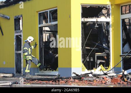 Quedlinburg, Deutschland. Juli 2021. Ein Feuerwehrmann geht in den ausgebrannten Supermarkt. In der Nacht waren etwa 77 Feuerwehrleute vor Ort, um den Markt kontrolliert verbrennen zu lassen. Die Brandursache und die Schadenhöhe sind noch nicht bekannt. Quelle: Matthias Bein/dpa-Zentralbild/dpa/Alamy Live News Stockfoto