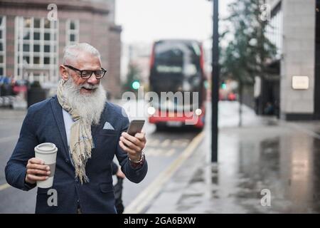 Leitender Geschäftsmann, der mit dem londoner Busbahnhof im Hintergrund Kaffee trinkt – Fokus auf das Gesicht Stockfoto