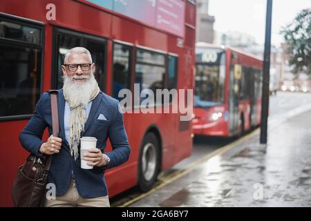 Leitender Geschäftsmann, der mit dem londoner Busbahnhof im Hintergrund Kaffee trinkt – Fokus auf das Gesicht Stockfoto