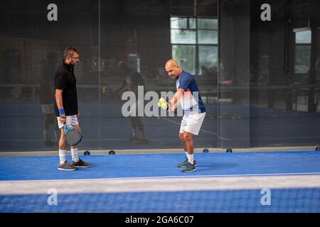 Überwachen Sie den Padel-Unterricht für den Mann, sein Schüler - Trainer lehrt Jungen, wie Padel auf dem Hallentennisplatz zu spielen Stockfoto