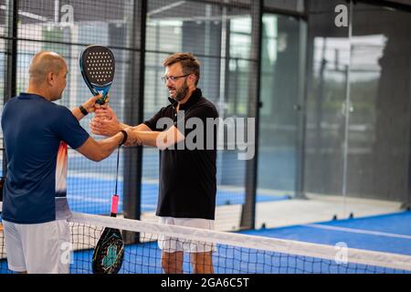 Überwachen Sie den Padel-Unterricht für den Mann, sein Schüler - Trainer lehrt Jungen, wie Padel auf dem Hallentennisplatz zu spielen Stockfoto