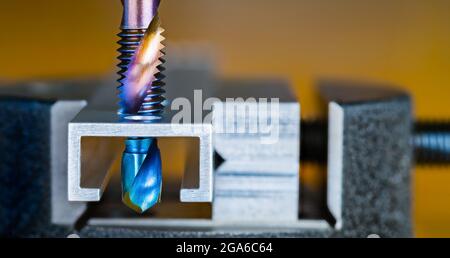 Stahlzapfen und Bohrer mit blau-violetter Nano-Titan-Beschichtung auf braunem Hintergrund. Zwei in einem. Bohren und Gewindebohren in Aluminium prof Stockfoto