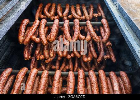 Nahaufnahme von geräucherten Würstchen aus Schweinefleisch und Rindfleisch, die in einem Holzraucherhaus hängen. Hausgemachte Produktion von getrockneten rauchigen Kielbasa. Leckere Wurstwaren. Stockfoto